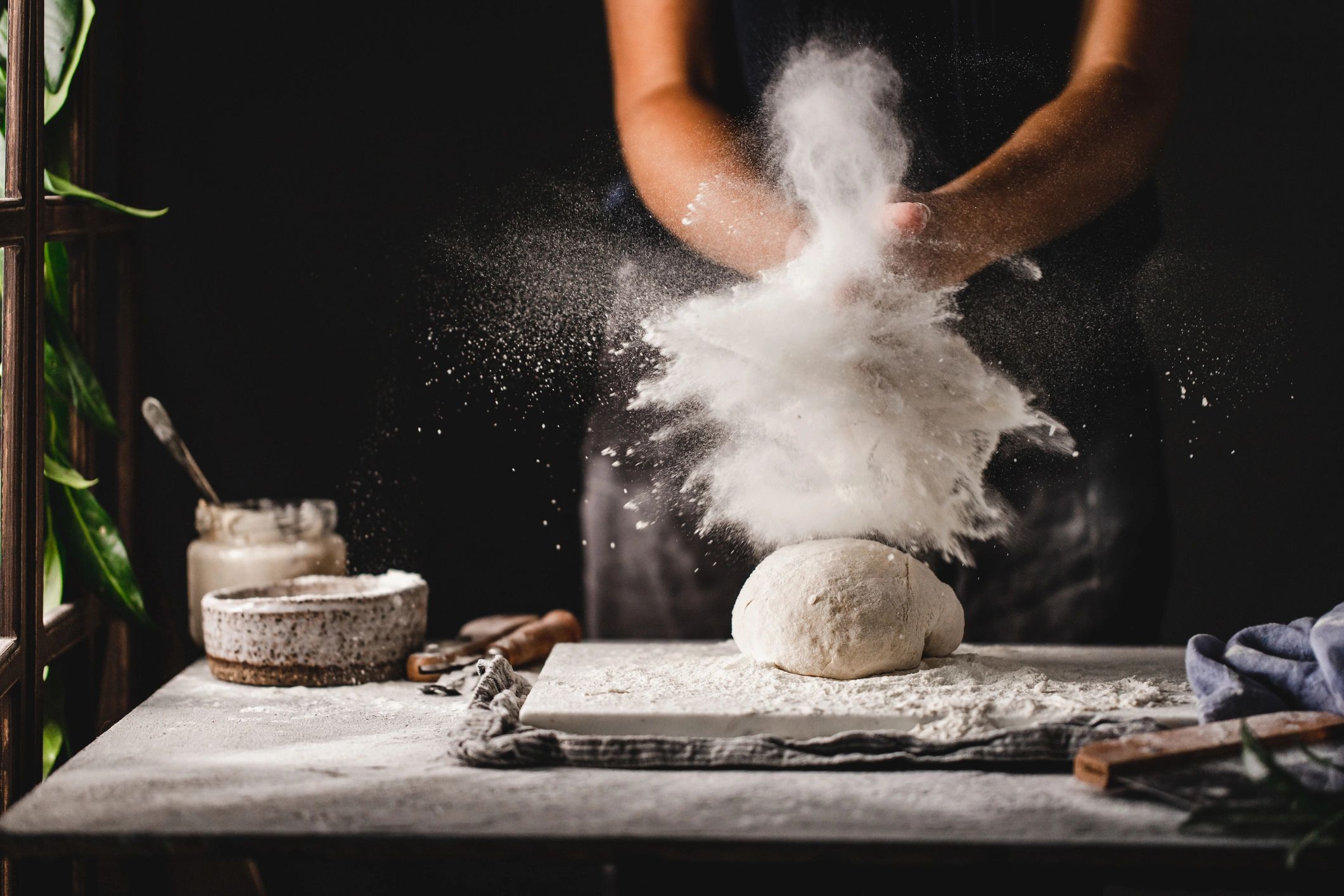 Hands dusting flour over dough while preparing bread