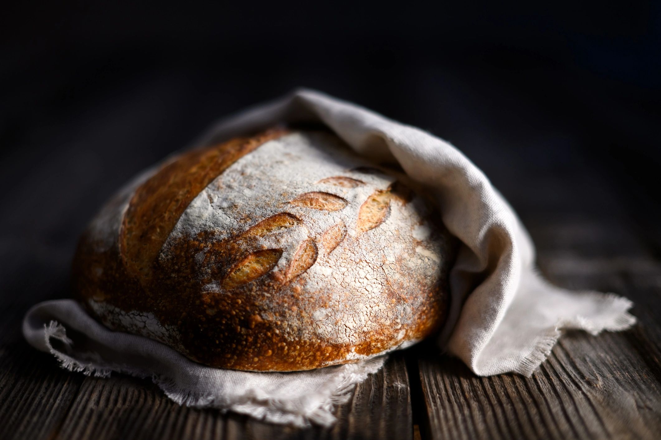 Close up of crusty leavened sourdough bread wrapped in a linen towel